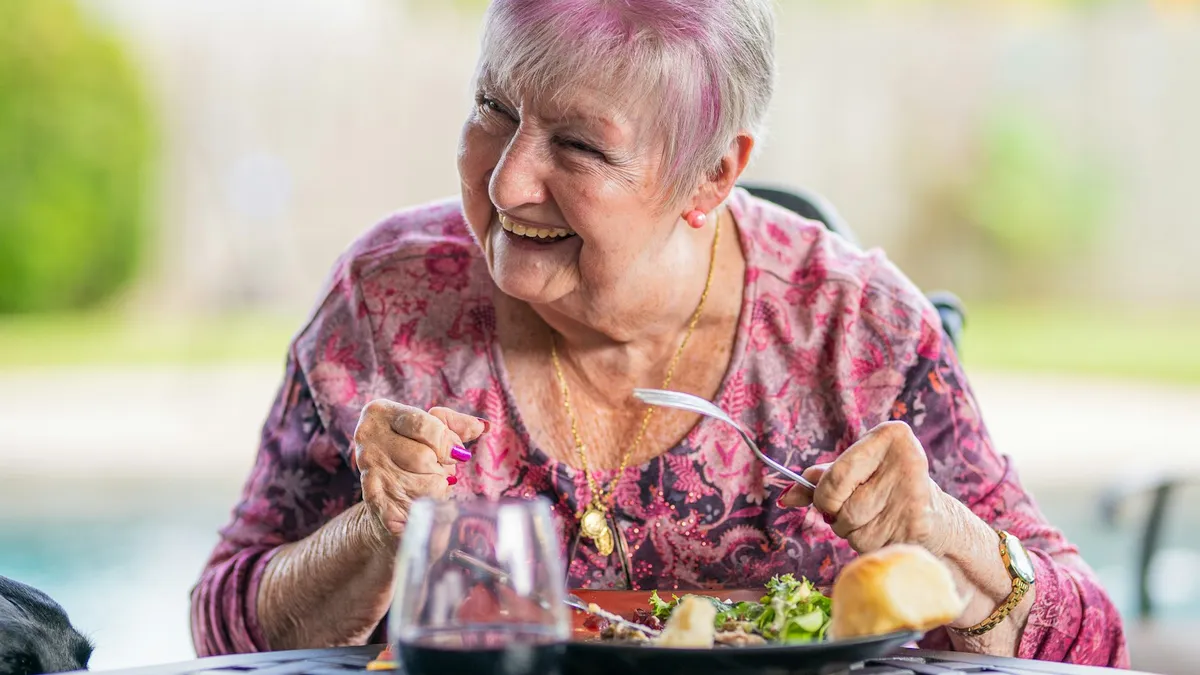 Oudere persoon en begeleider aan tafel tijdens de maaltijd in een dagverzorgingscentrum