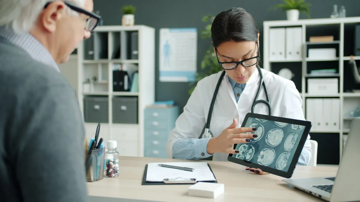 Oudere persoon bekijkt een tablet met een mantelzorger naast zich