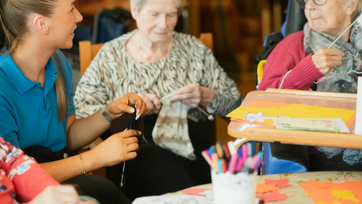 Oudere persoon krijgt thuis ondersteuning aan de keukentafel