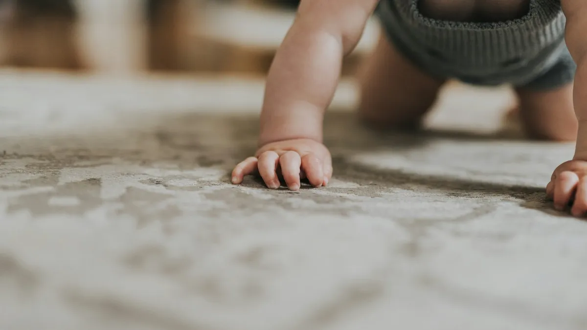 Ouder observeert een kruipende baby op een speelkleed thuis