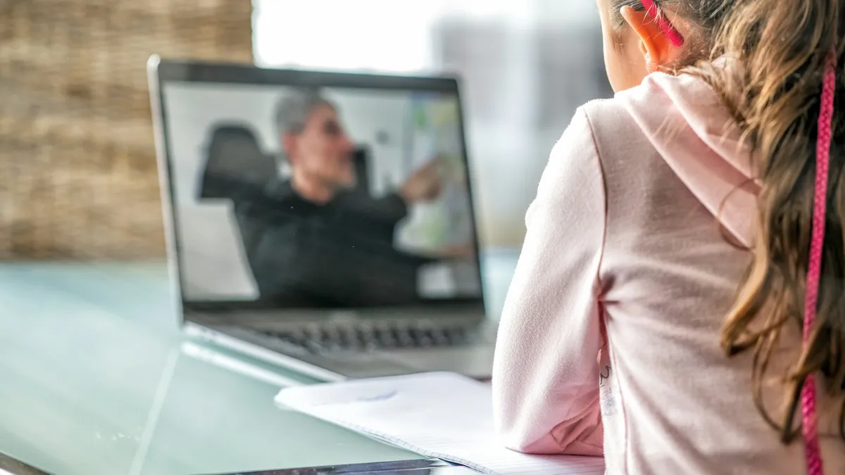Persoon volgt een online logopediesessie aan een laptop met oefenmateriaal op tafel