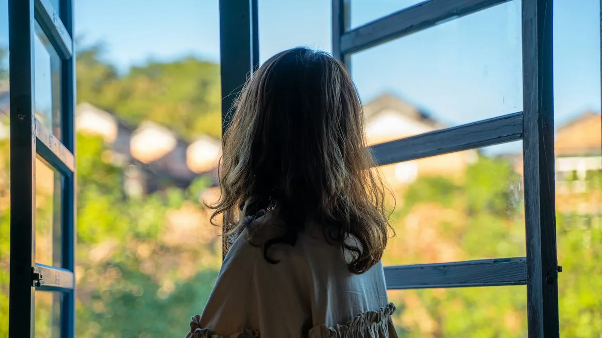 Vrouw van middelbare leeftijd zit rustig aan een raam met een kop thee tijdens de overgang
