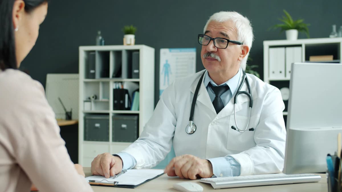 Persoon die vermoeid aan een keukentafel zit met een glas water en notitieboek