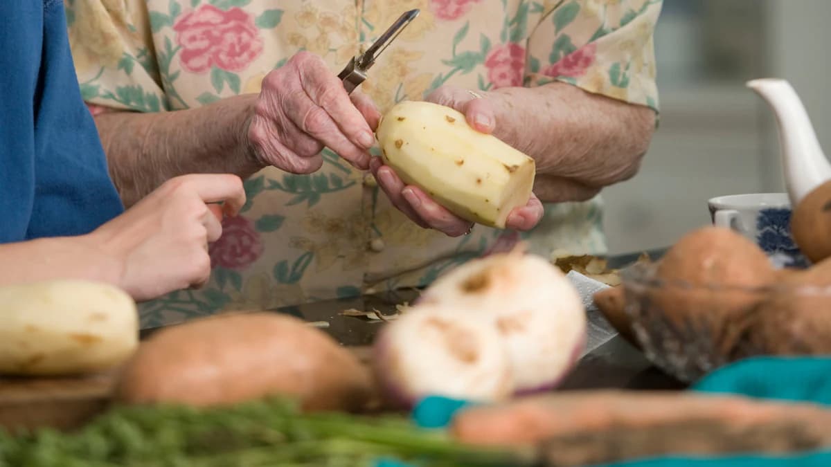 Mantelzorger helpt een oudere persoon aan tafel met een voedzame maaltijd