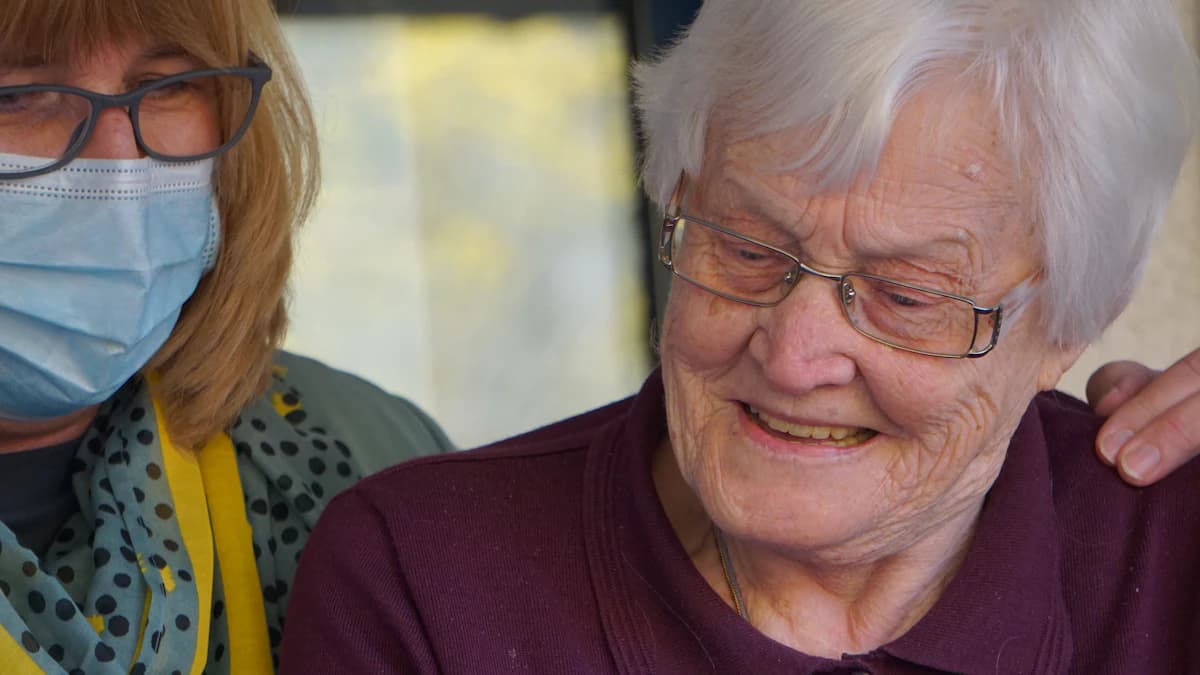 Thuisverpleegkundige bespreekt een zorgplan met een oudere persoon en mantelzorger aan de keukentafel